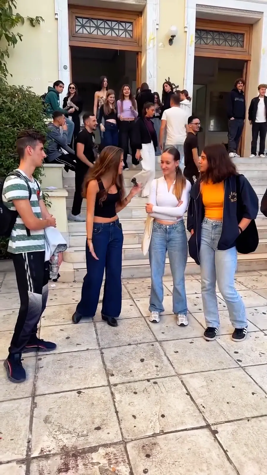 Students answering quiz questions on the steps of a university in Athens.