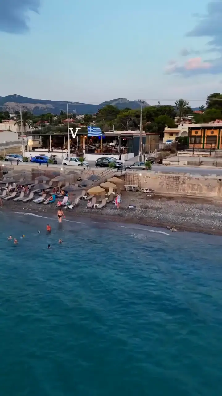 Swimmers and sunbeds in front of a beach bar at golden hour, filmed from the drone.