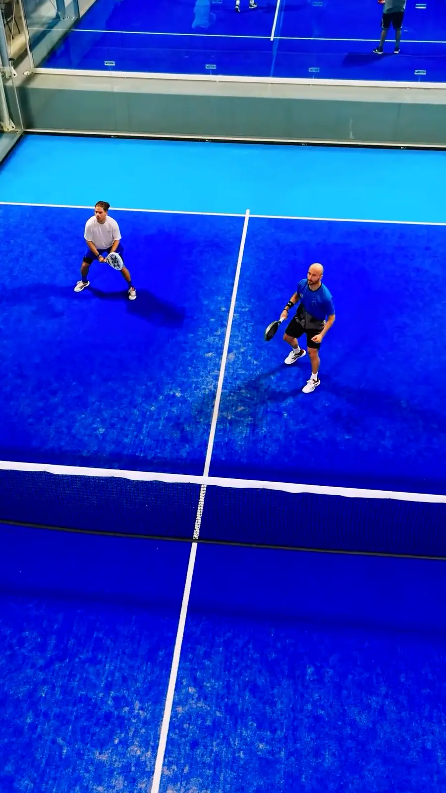 Padel players on a blue court, filmed from the drone.